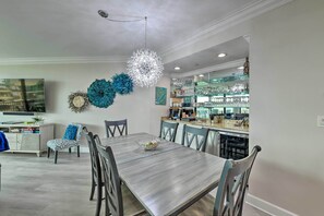 A modern kitchen with a bar area, featuring a large dining table, chairs, and a hanging light fixture.