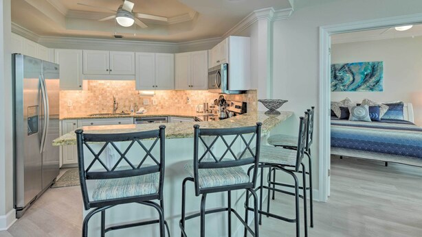 A modern kitchen with white cabinets, a stainless steel refrigerator, and a center island with bar stools. - Top Floor Condo w/ Resort-style Amenities! (Orange Beach)