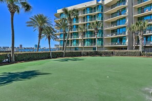A golf course with a view of a multi-story hotel with balconies and palm trees.