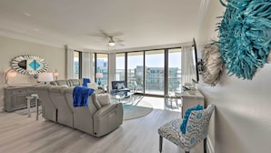 A spacious living room with a gray sofa, a patterned armchair, and a dining area with a glass table. - Top Floor Condo w/ Resort-style Amenities! (Orange Beach)