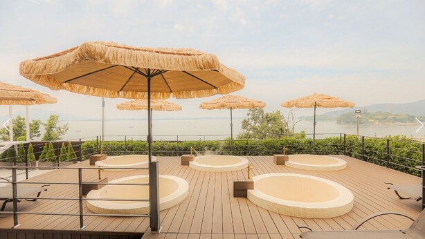 Una terraza en la azotea con sombrillas de paja, jacuzzis y vistas al mar.