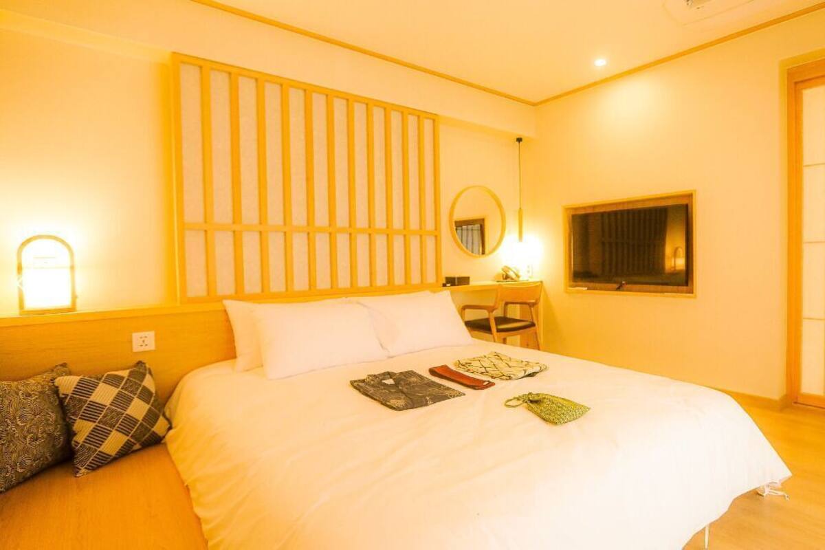 Ein Hotelzimmer mit Bett, Nachttisch, Lampe, Spiegel und einer Schiebetür.