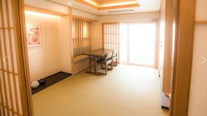 Una habitación tradicional japonesa con suelo de tatami, una mesa baja con sillas, puertas correderas y un panel shoji.