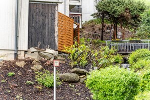 A building with a wooden gate, a small waterfall, and a garden with various plants and rocks.