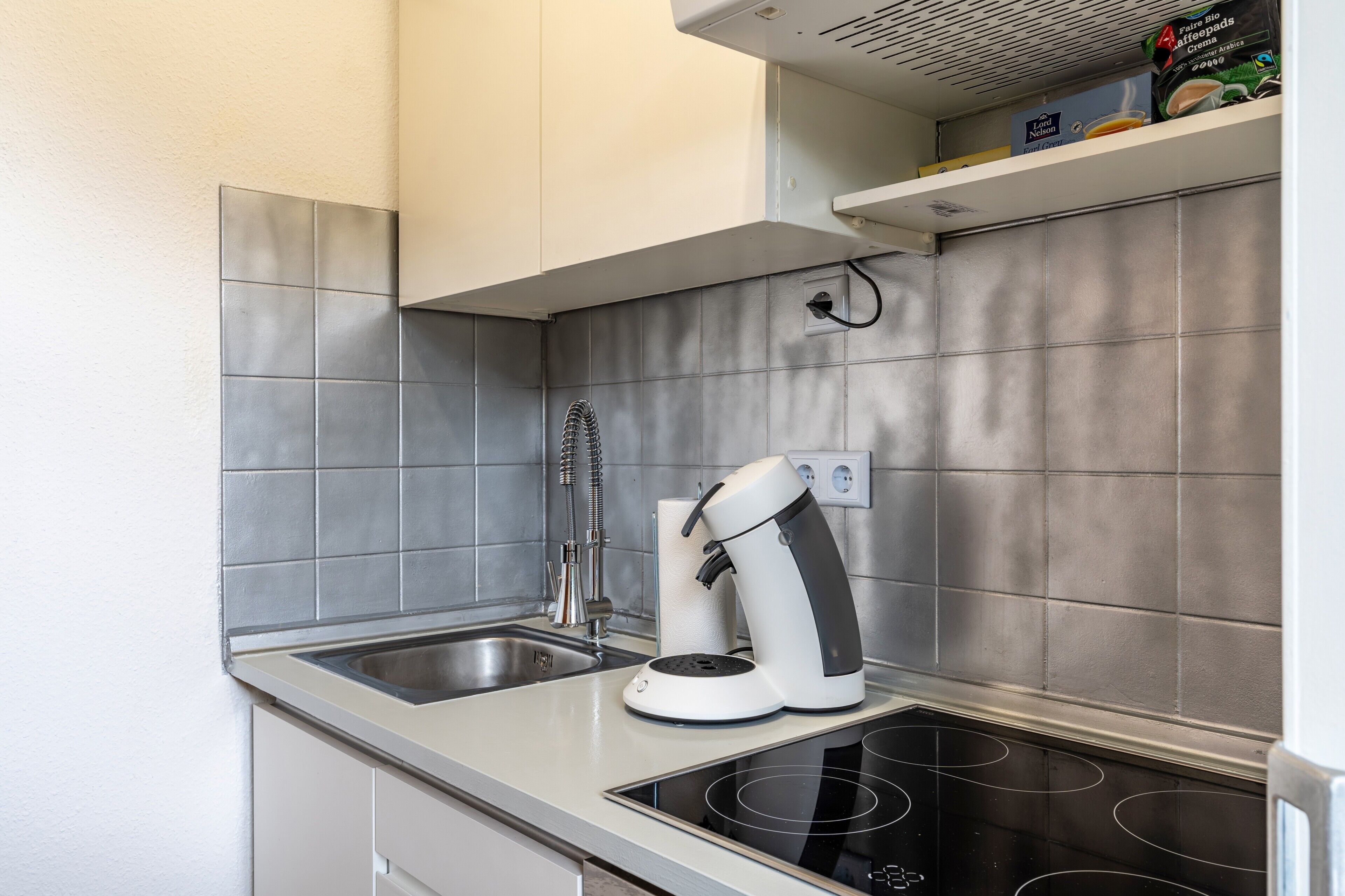 Une cuisine moderne dotée d’une plaque de cuisson intégrée, d’une machine à café et d’un évier en acier inoxydable.