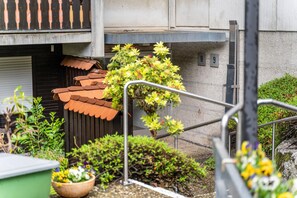 Une cour avec un toit en tuiles, des plantes en pot et une rambarde en métal.