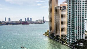 Un edificio alto con vista al agua, un puerto deportivo con barcos y un puente al fondo.