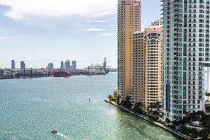 Un edificio alto con vista al agua, un puerto deportivo con barcos y un puente al fondo.