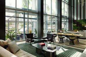 A modern hotel lobby with a large glass window, a sofa, chairs, a coffee table, and a small dining area.