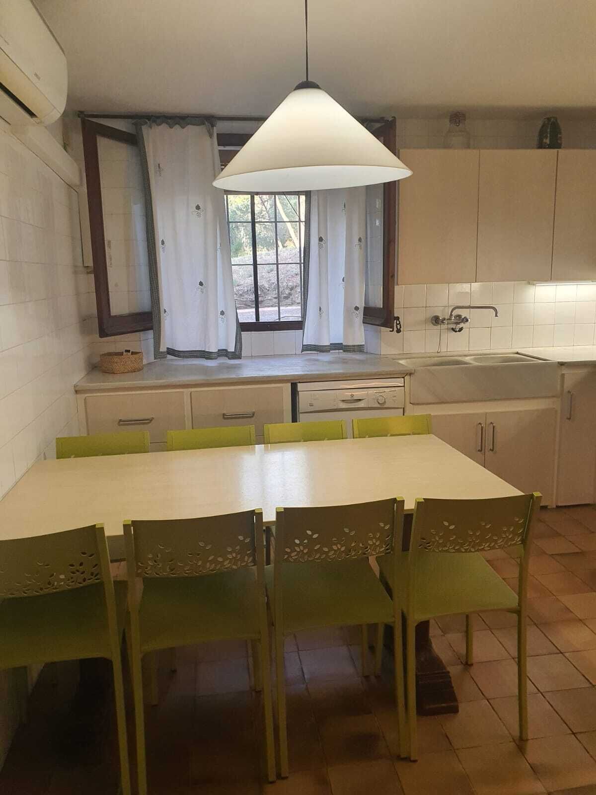 Una cocina con una mesa de comedor, sillas, una ventana con cortinas y una lámpara colgante.