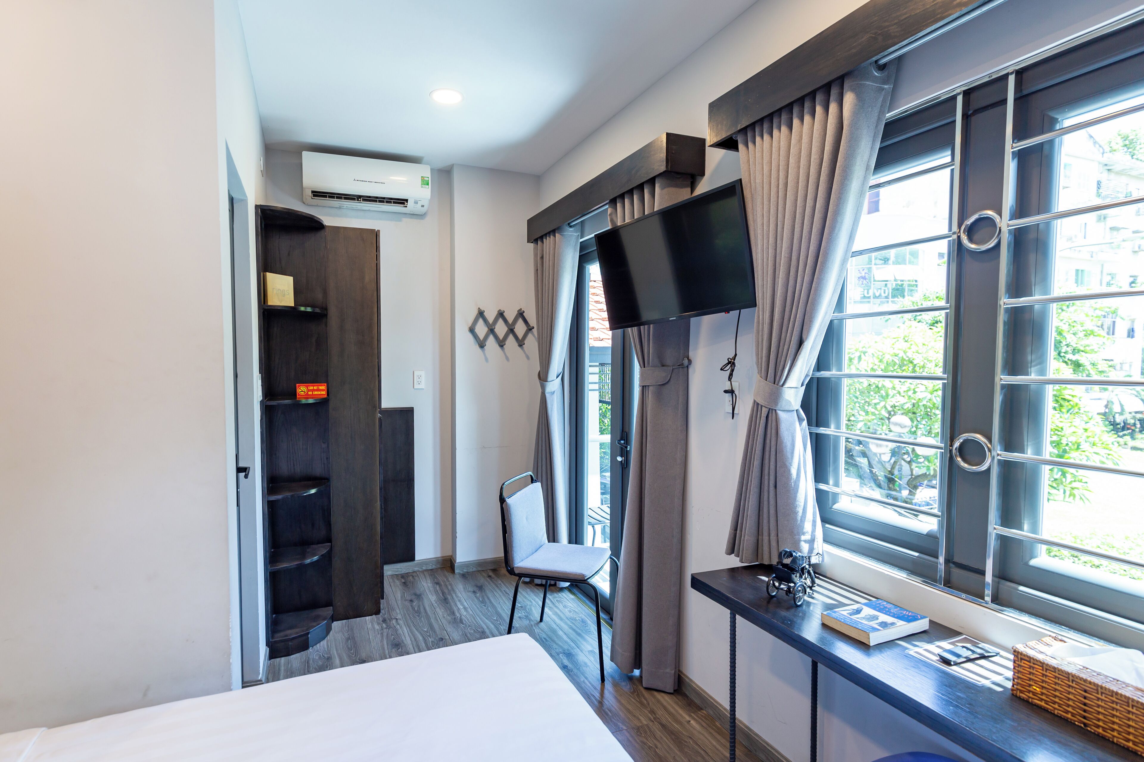 A hotel room with a bed, a desk with a computer, a TV, and a window with curtains.
