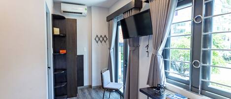 A hotel room with a bed, a desk with a computer, a TV, and a window with curtains.