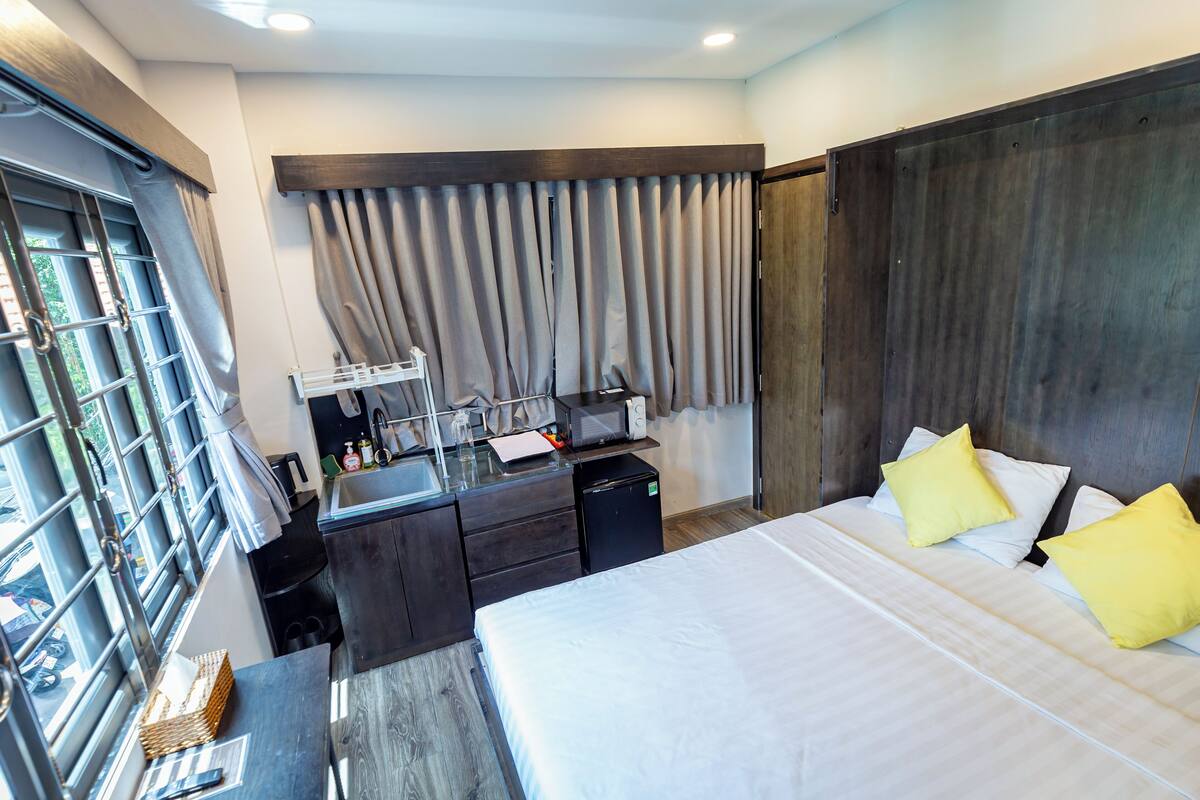 Une chambre d’hôtel moderne, dotée d’un grand lit, d’un bureau avec un ordinateur, d’un petit réfrigérateur et d’une fenêtre avec des rideaux.