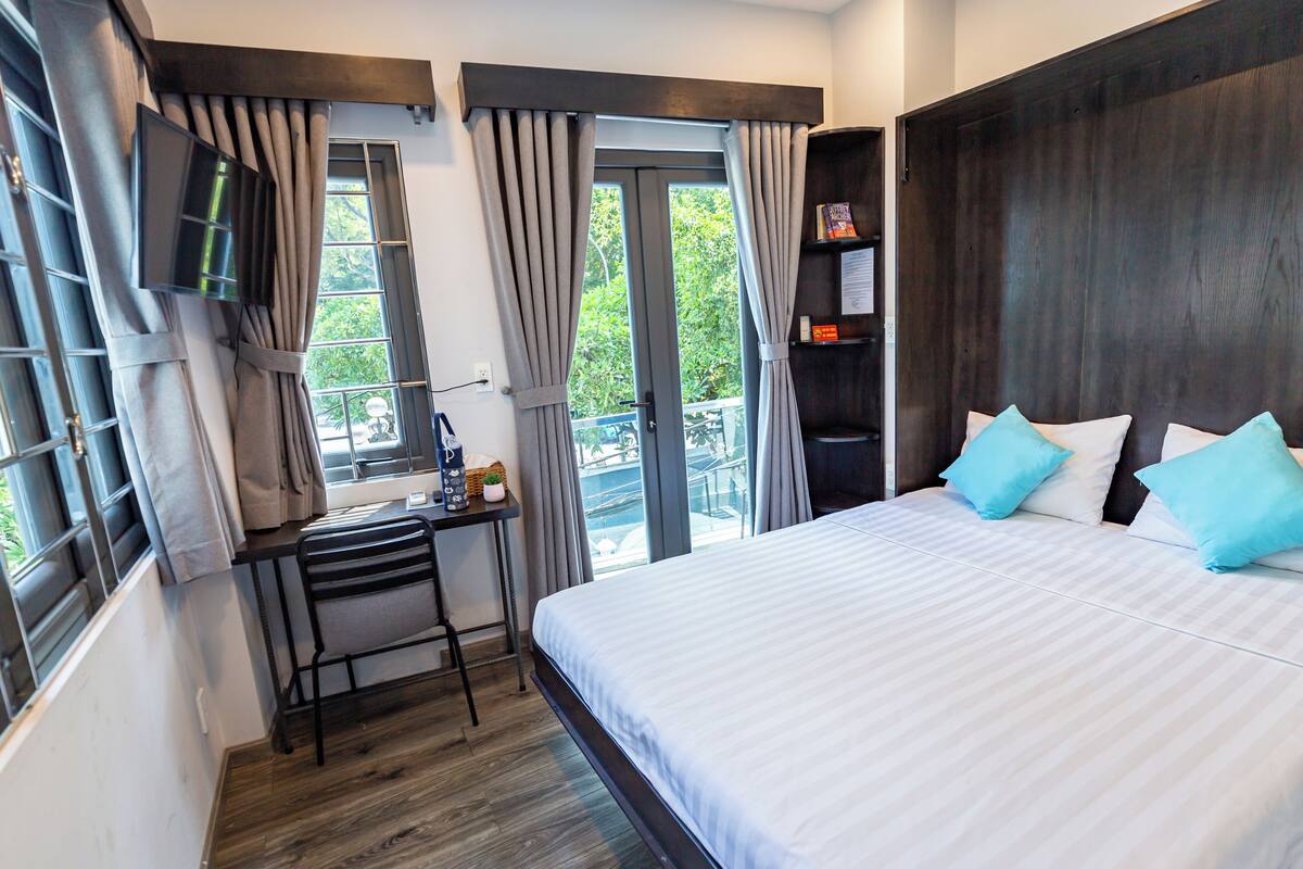 Une chambre à coucher avec un lit, un bureau, une télévision et une fenêtre avec des rideaux.