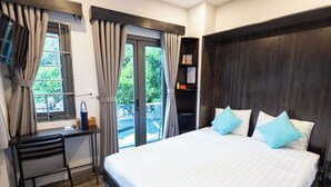 A bedroom with a bed, a desk, and a view of greenery outside.