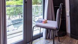 A room with a sliding glass door, a chair, a small shelf with a book, and a dark wooden wardrobe.