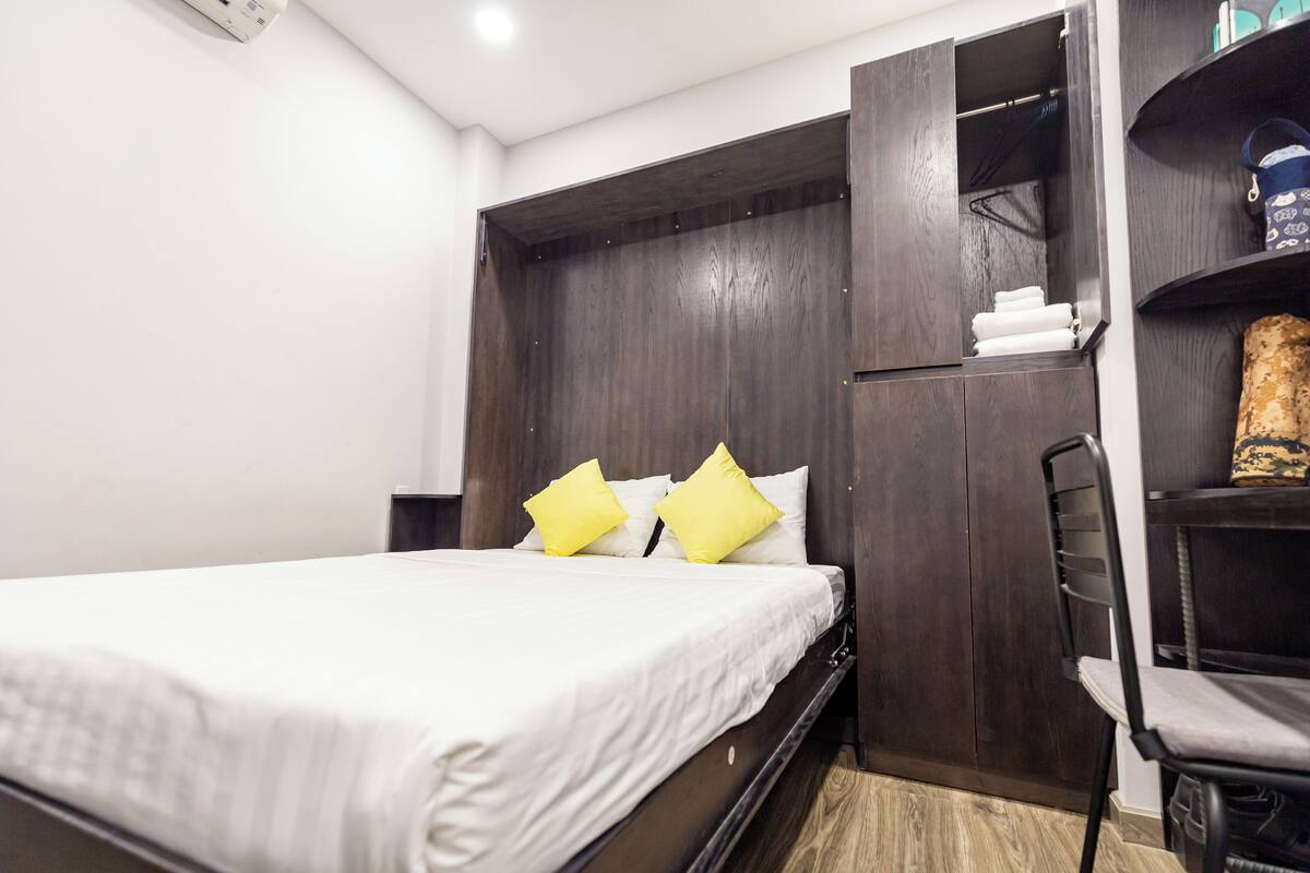 Une chambre à coucher comprenant un lit, une armoire en bois, une chaise et une étagère avec divers objets.