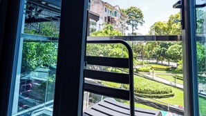 A balcony with a metal bench, a glass door, and a view of a park and buildings.