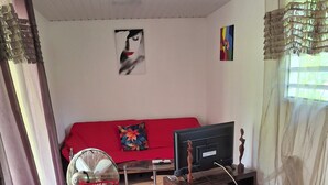 A living room with a glass-top dining table, red chairs, a red sofa, a television, and a decorative wall piece. - Island colors (REMIRE MONTJOLY)