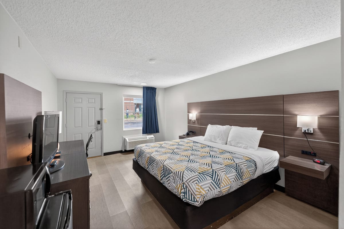 A hotel room with a bed, bedside table, TV, and a window with curtains.