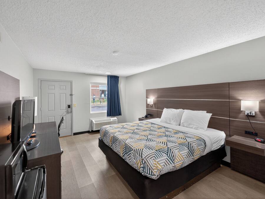 A hotel room with a bed, bedside table, TV, and a window with curtains.
