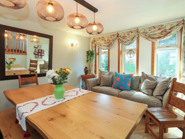 A dining area with a wooden table, chairs, a vase of flowers, and a sofa with patterned cushions.