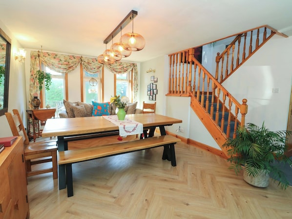 Un espace repas comprenant une table en bois, des bancs et un escalier avec des rampes en bois.