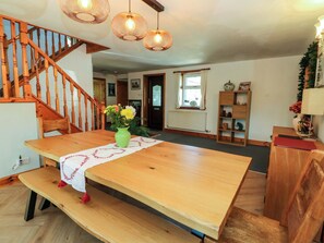 A wooden dining table with a vase of flowers, a bench, a staircase, and a bookshelf.