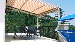 A covered outdoor seating area with tables and chairs, a blue pool, and a view of greenery. - Vacation home with private grounds and pool with panoramic views in Tremosine (Tremosine)