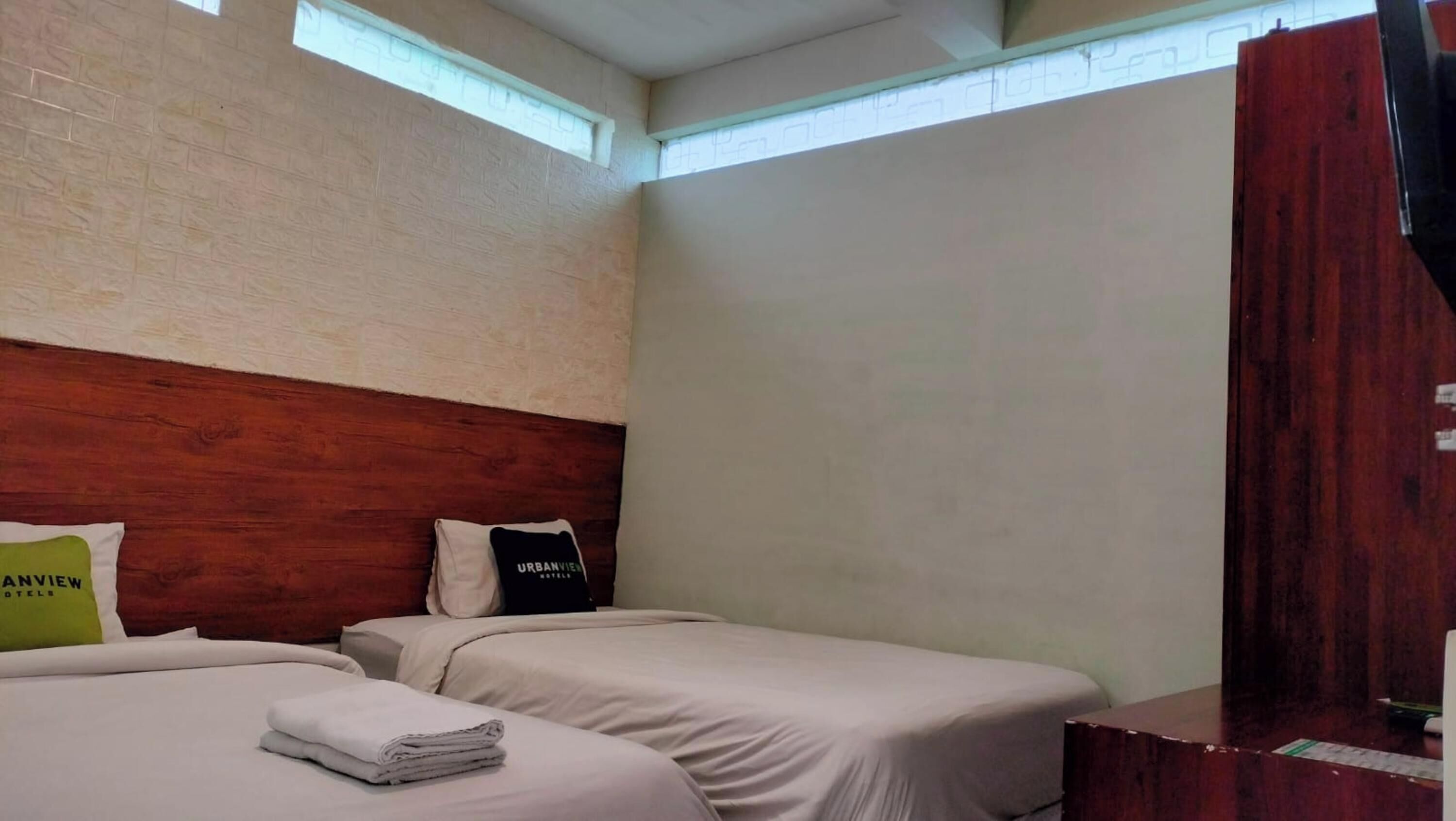 Ein Hotelzimmer mit zwei Betten, einem Holzkopfende, einem Fenster und einem Holzschrank.
