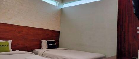 A hotel room with two beds, a wooden headboard, a window, and a wooden wardrobe.