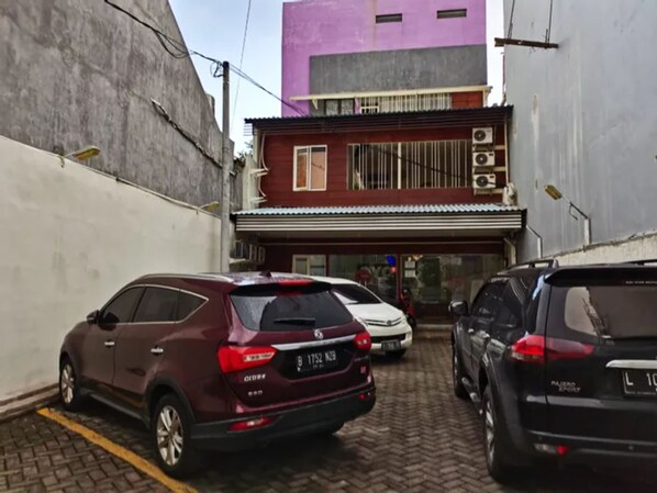 A parking area with cars, a building with a purple facade, and a white wall. - Kozy 15 Guesthouse (Surabaya)
