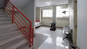 Un couloir propre et bien éclairé, avec un escalier rouge, un espace d’attente doté de chaises et une petite table.