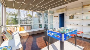 A room with a foosball table, a sofa with cushions, a bookshelf, and large windows. - Penthouse with terrace Navigli Bocconi - NavigliApartments  (Milano)