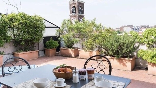 A rooftop terrace with a table set for breakfast, potted plants, and a clock tower in the background. - Penthouse with terrace Navigli Bocconi - NavigliApartments  (Milano)