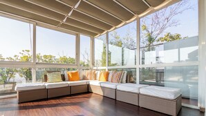 A covered outdoor seating area with a large window, wooden flooring, and a view of trees. - Penthouse with terrace Navigli Bocconi - NavigliApartments  (Milano)