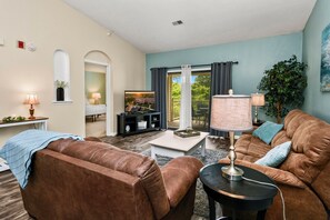 A living room with a brown leather sofa, a coffee table, a TV, and a lamp.