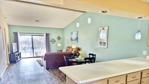 A spacious living area with a large sofa, dining table, and kitchen area with cabinets.