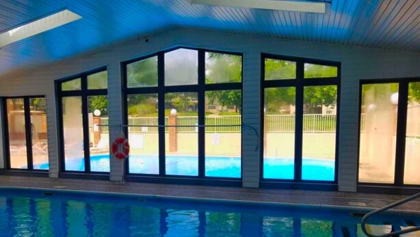 An indoor swimming pool with large windows, a lifebuoy, and a poolside area visible through the windows.