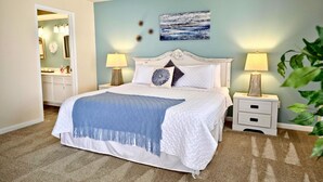 A bedroom with a bed, two bedside tables, a nightstand, a mirror, and a painting on the wall.