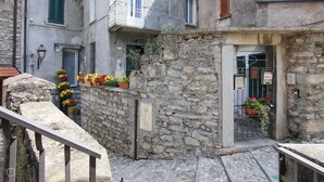 A stone building with a narrow entrance, a metal gate, and flower boxes on the ledge. - Italianway - Riva Soldino 9 (Laglio)