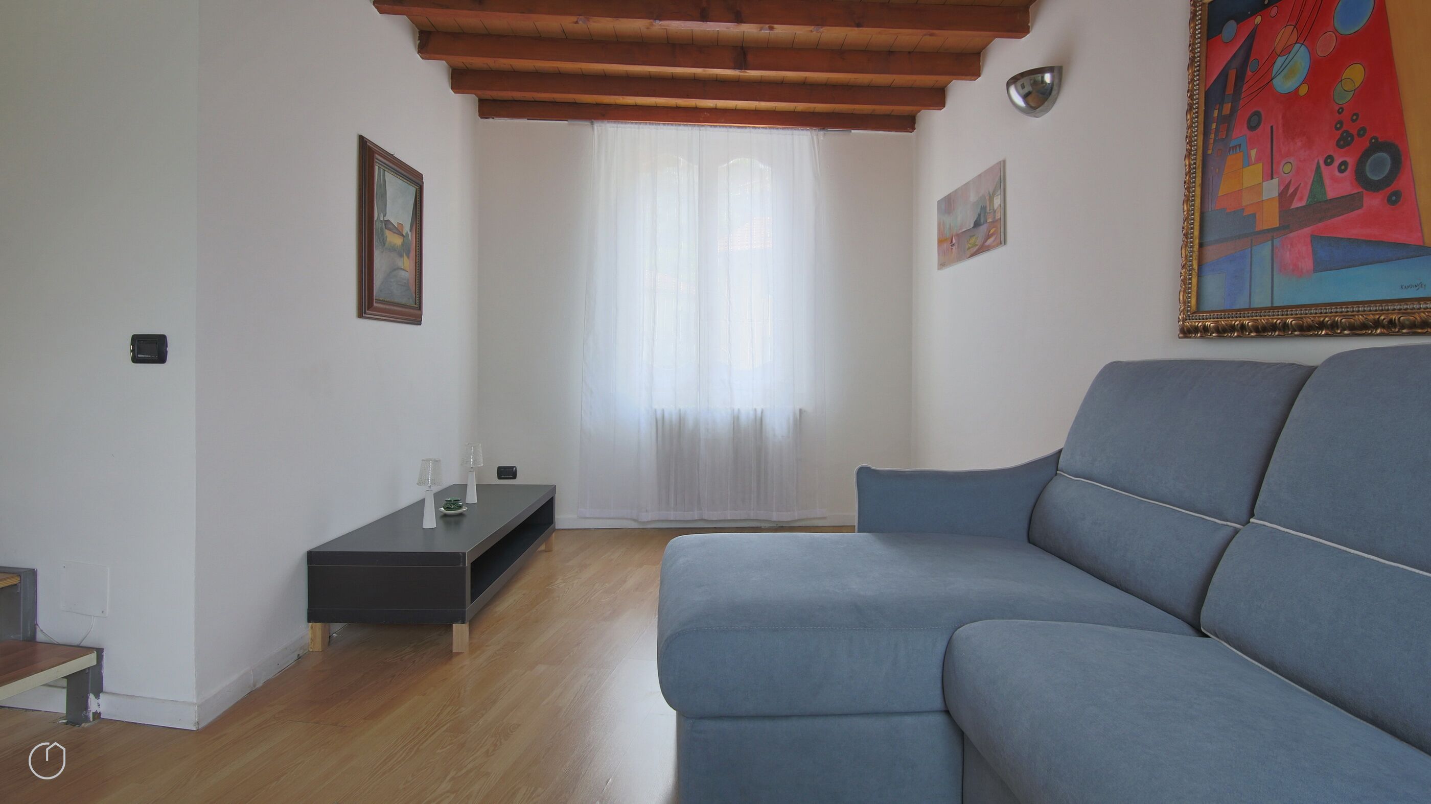 A modern living room with a blue sofa, a dark wooden coffee table, and a white curtain.