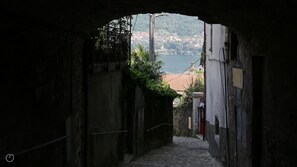 A narrow stone pathway leading to a scenic view of a lake and buildings in the distance. - Italianway - Riva Soldino 9 (Laglio)