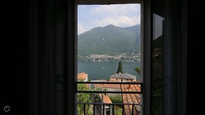 A view through a window of a lake with a mountain in the background and a town across the water. - Italianway - Riva Soldino 9 (Laglio)
