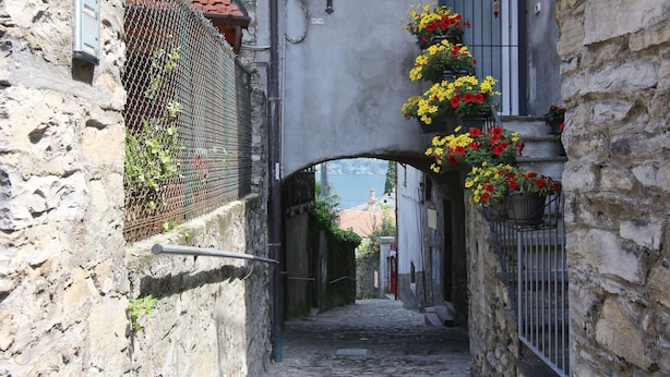A narrow stone alleyway with a metal gate and flower baskets on the right. - Italianway - Riva Soldino 9 (Laglio)
