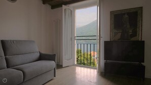 A living room with a grey sofa, a TV, and a balcony with a view of a lake and mountains. - Italianway - Riva Soldino 9 (Laglio)