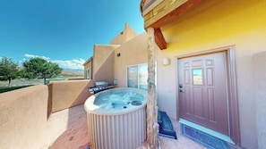 Un jacuzzi al aire libre frente a un edificio con terraza de madera y una puerta.