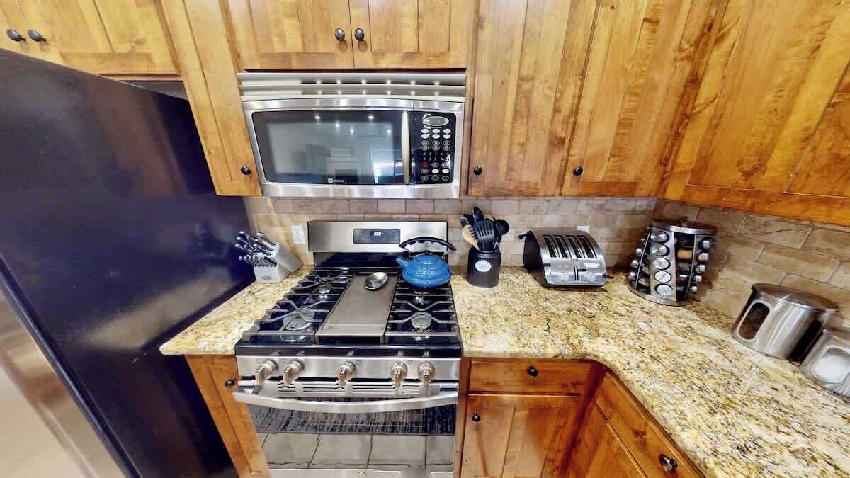 Une cuisine avec des meubles en bois, un four à micro-ondes en acier inoxydable, une cuisinière à gaz, un grille-pain et un évier.