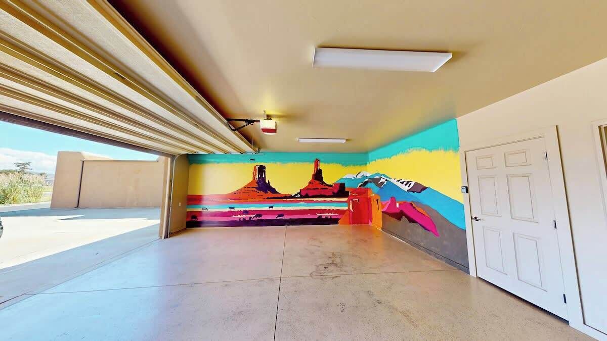 Ein Zimmer mit großem Fenster, einer Tür und einem farbenfrohen Wandgemälde.