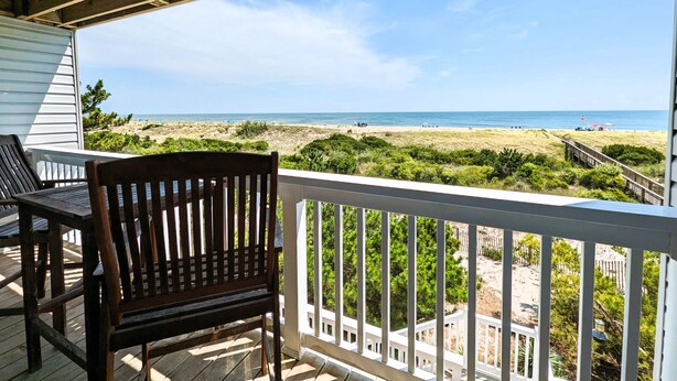Une terrasse en bois avec vue sur la plage, une chaise et une rambarde.